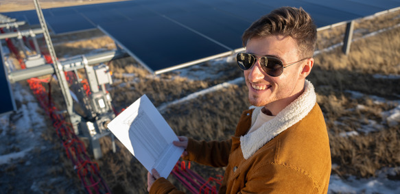 A Wyoming EPSCoR researcher smiles in front of a solar panel outside on the plains.