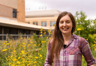 A UW researcher stands and smiles in front of a a UW building and flower display.