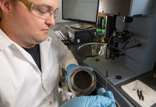A University of Wyoming researcher carefully measures out a dark powdered substance in a lab.