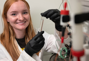 A Wyoming EPSCoR researcher smiles as they hold a vial in a lab at the University of Wyoming.