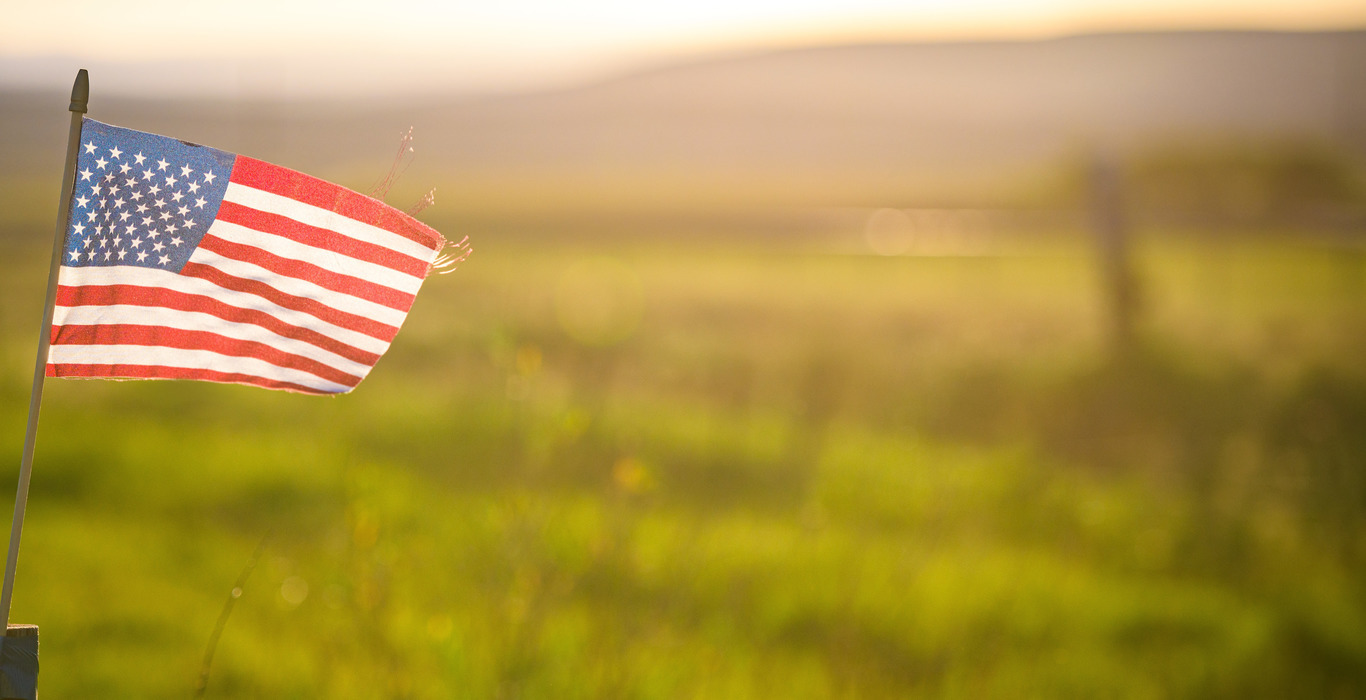 small american flag taped to fence post in front of grass feild