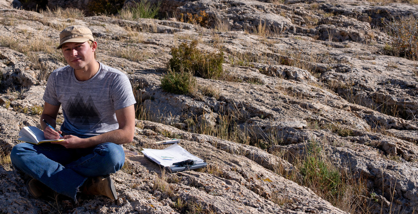 Student brayden green works in notebook sitting on rocks as a part of the geology 2800 course
