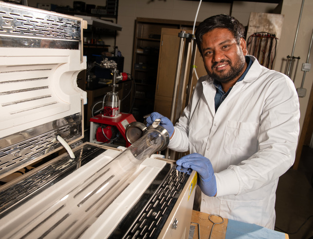 Researcher in lab coat and gloves next to machine