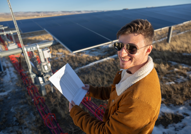 Man smiling holding papers next to solar panels