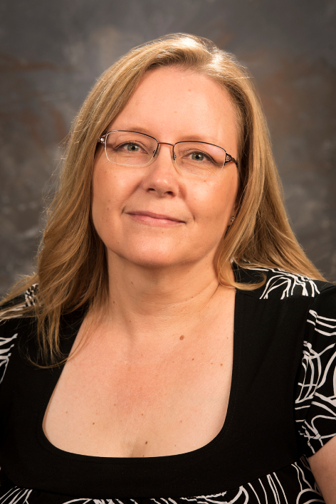woman with long hair and white and black shirt looks at camera
