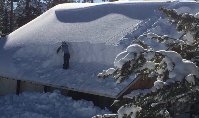 Image of a AMK ranch facility employee removing snow from a rooftop of one of the lodges at AMK Ranch