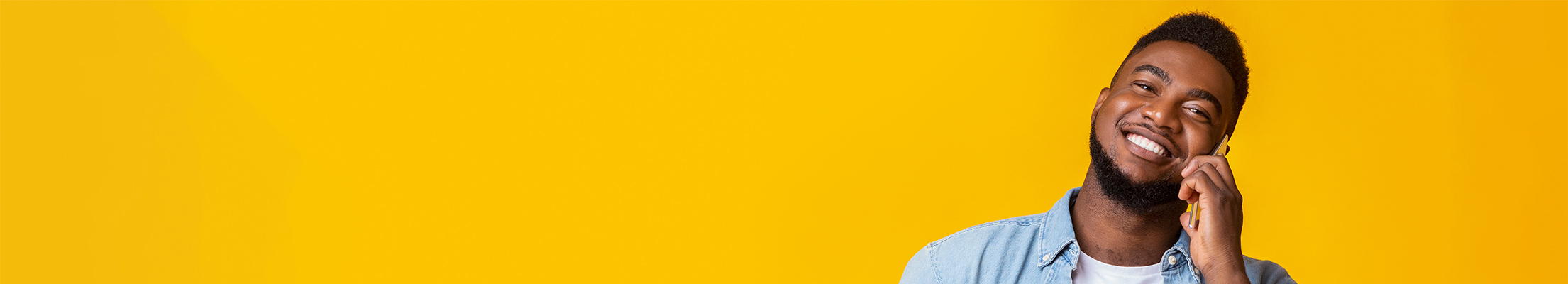 Smiling young black man holding mobile phone on a yellow background