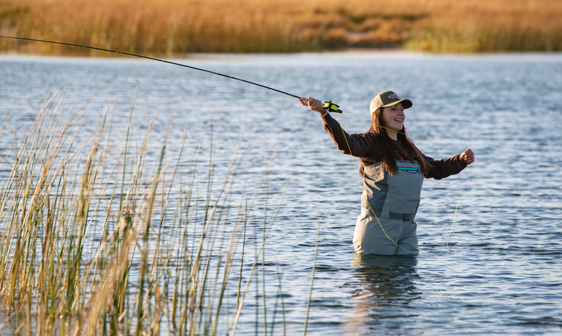 Young woman standing in a stream fly fishing