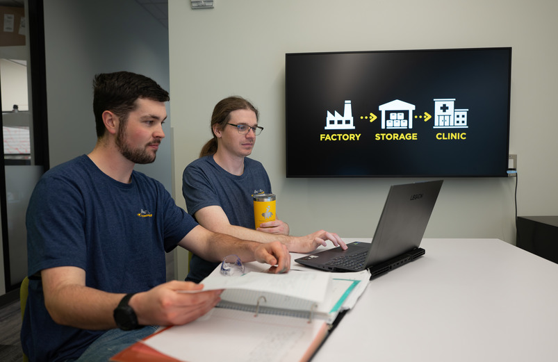 tyler gonzalez and carter wiberg look at a laptop with the graphic in the background that says factory storage clinic