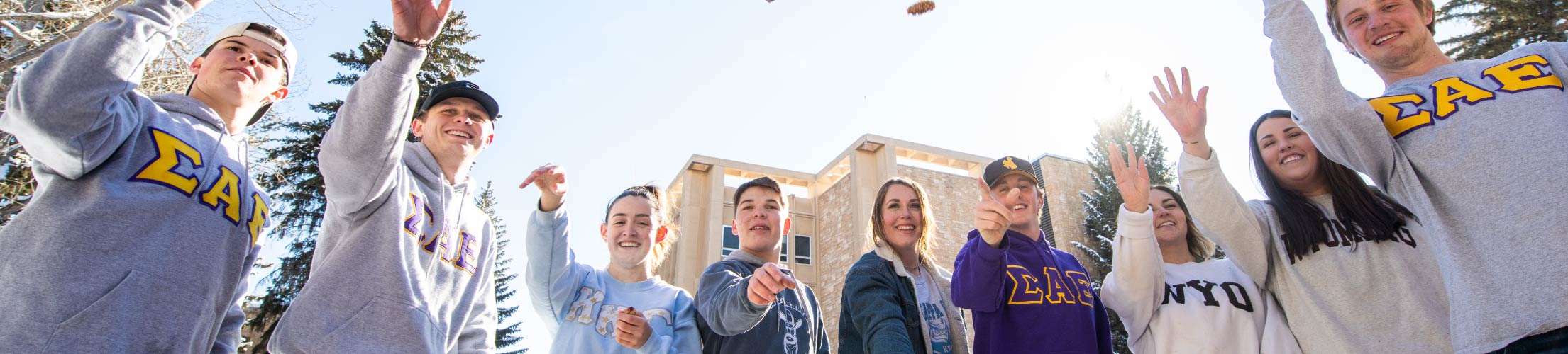 Students stand in a row throwing spruce cones into the air.