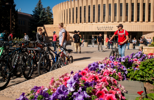 Students stand by a bicycle rack and the UW Classroom Building in the springtime