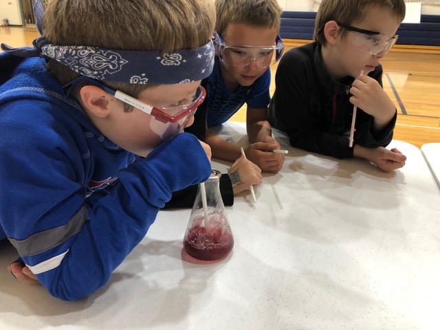 Student blowing bubbles through a straw into an erlenmeyer flask