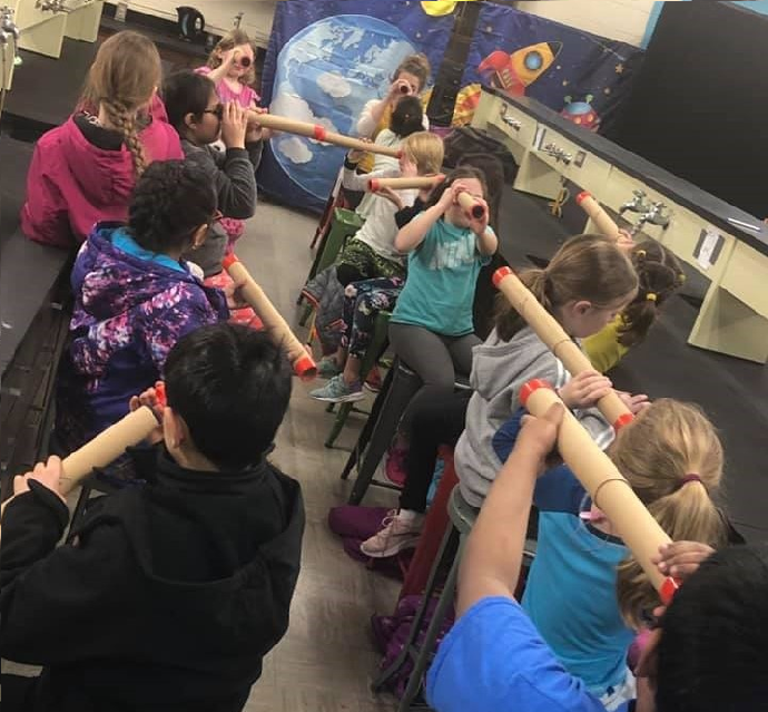 Students looking around the room with the cardboard telescopes that they made