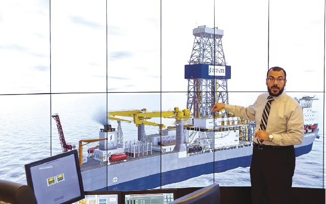 Tawfik standing in front of a large petroleum boat being projected on a screen