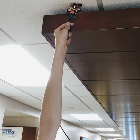 Student reaches for a microbit hidden in the ceiling