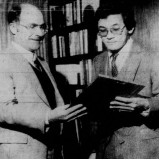 Older photo of Dr. Fuji Adachi and colleague holding a book. 