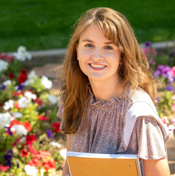 SSS student poses for a picture while holding a notebook in her arm with flower bed in the background.