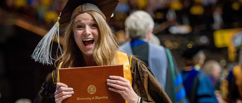 Student posing with her diploma and smiling during a UW commencement ceremony.