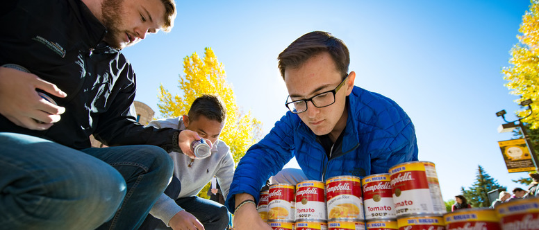 Three students helping to stack cans of soup.