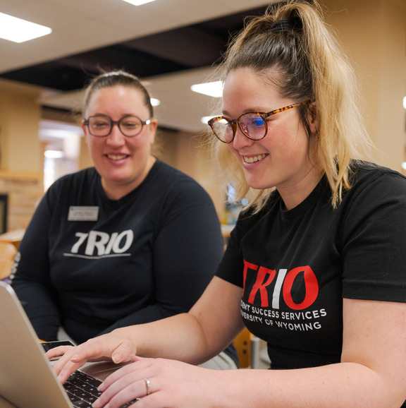 Two TRIO staff members working together on a laptop. 