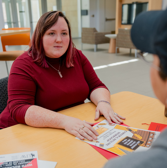 TRIO staff member speaking to a student over an event poster.