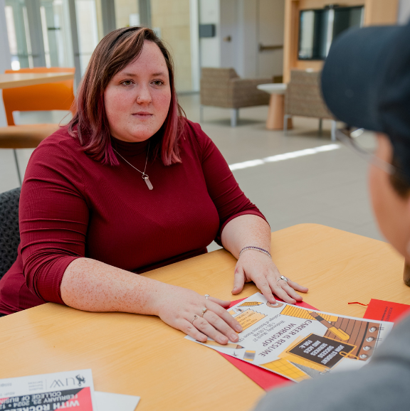 TRIO staff member speaking to a student over an event poster. 