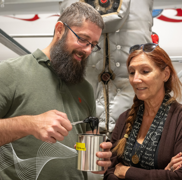 Two people in a lab looking at a container of a thick substance
