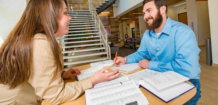 Two students study together at a table covered in books