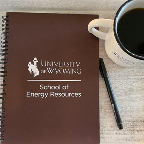 a brown notebook with the SER logo on the cover next to a cup of coffee and a pen