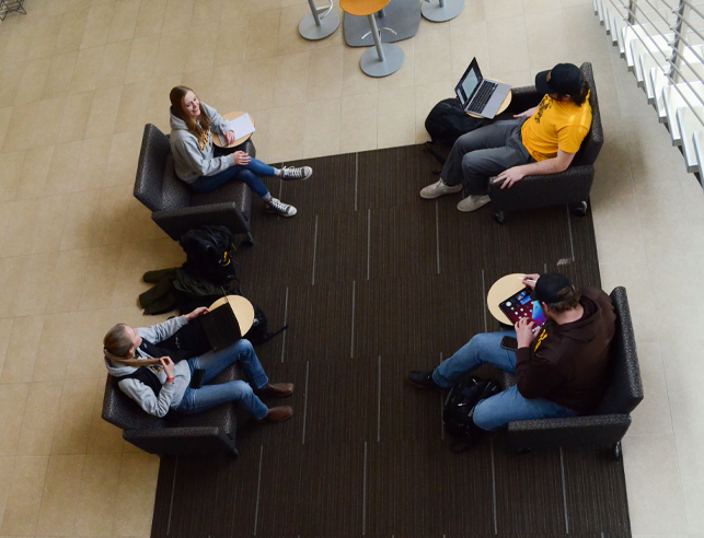 Students talking on top of stairs in Energy Innovation Center holding a land book
