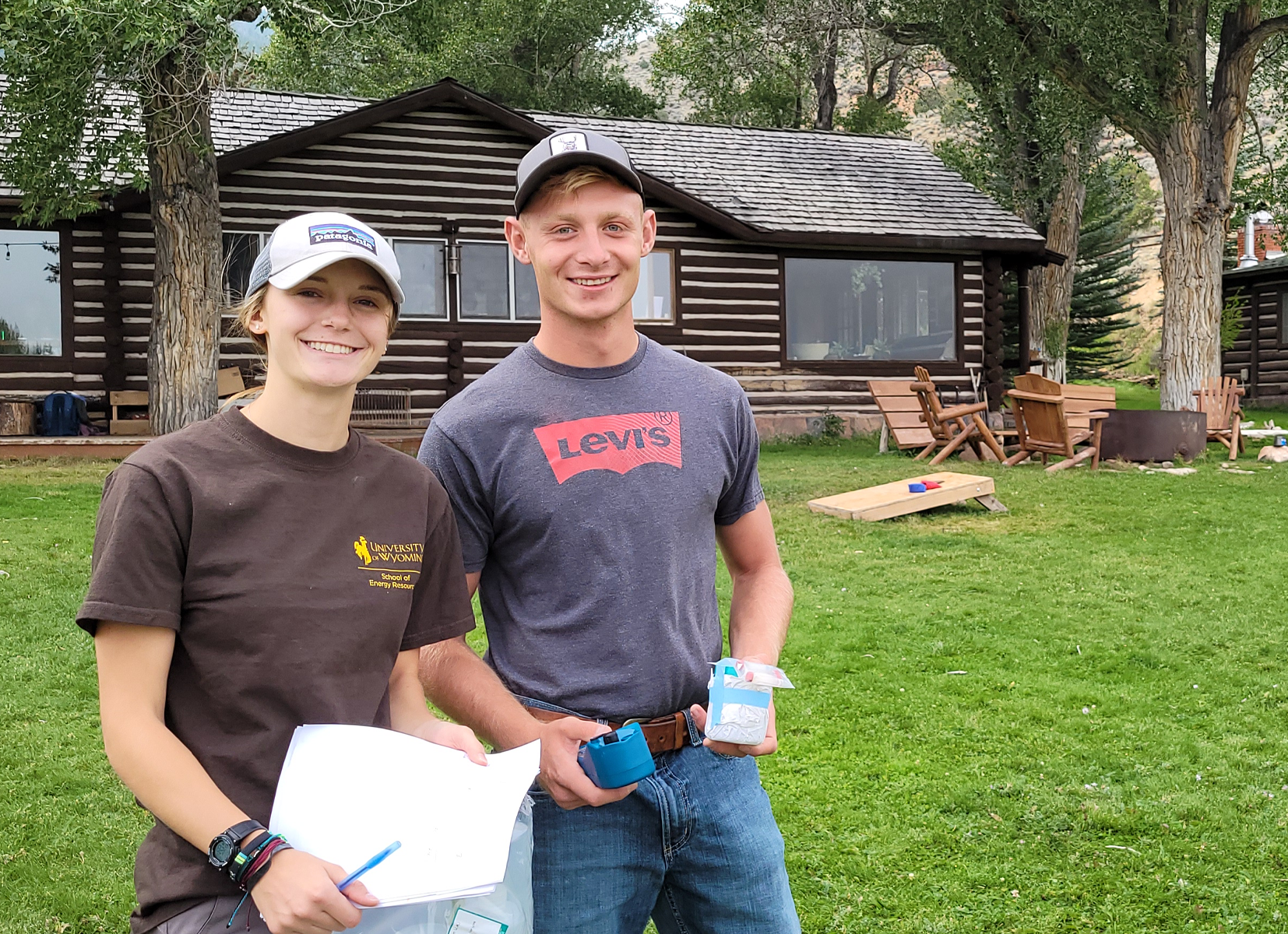 Two students on a green grassy hill taking water samples