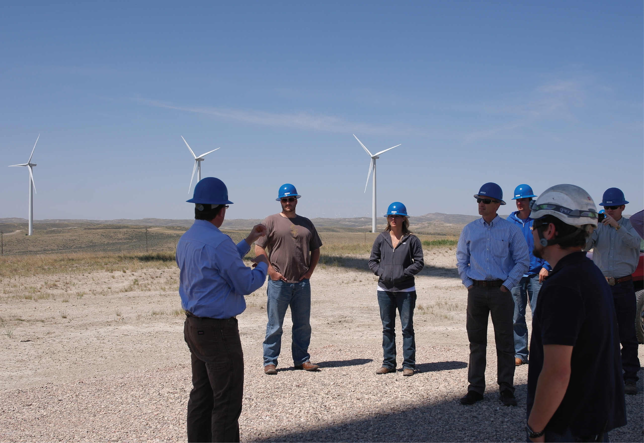 a group of people learning about wind energy with wind turbines in the distance