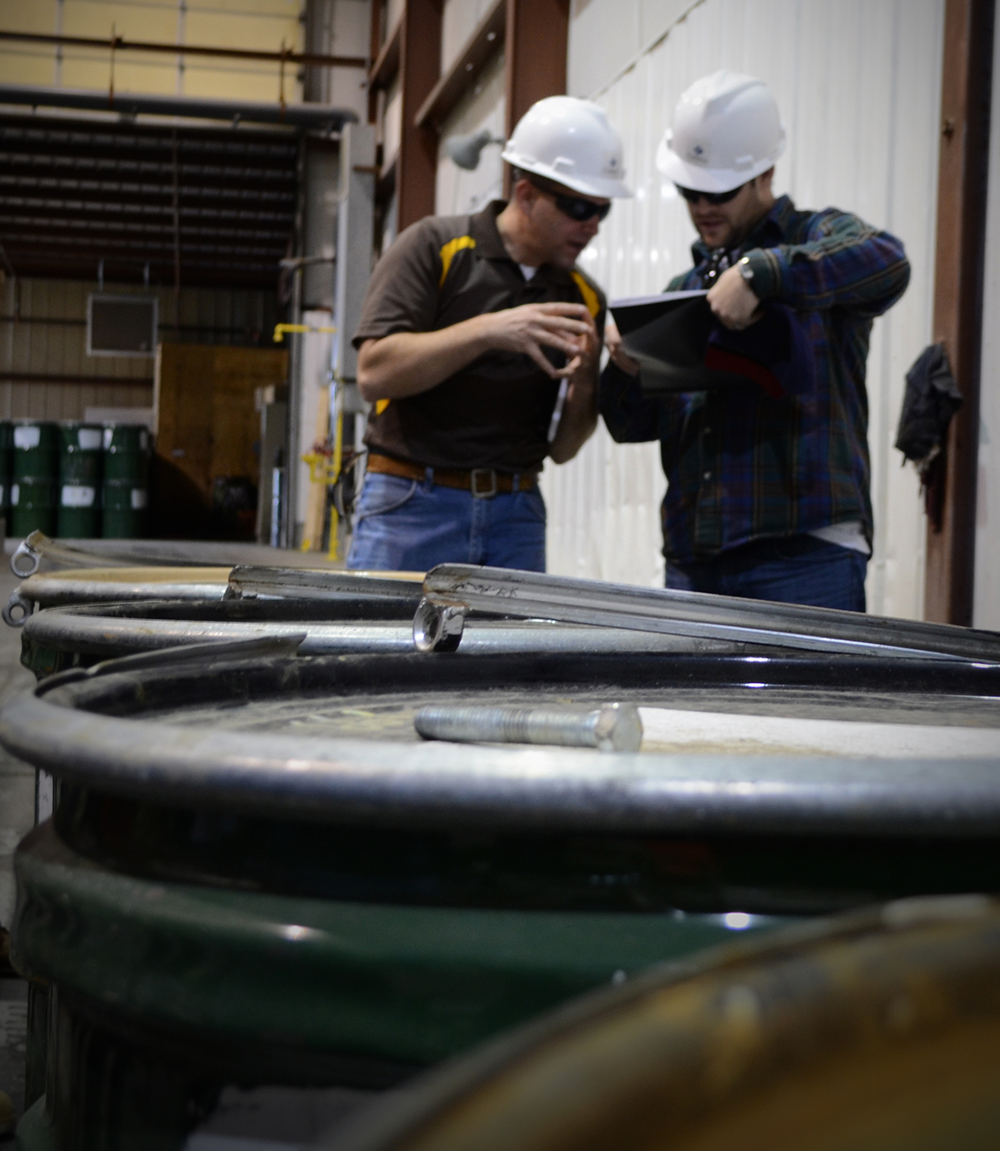 men in hard hats talking in front of uranium barrels