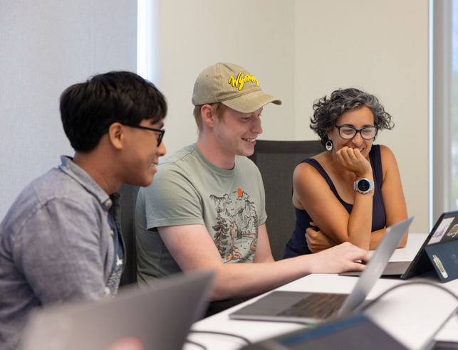 Student completing online forms on laptop with the assistance of two other people
