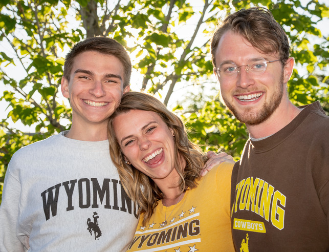 Three UW students smile for the camera in downtown Laramie with a background of trees.