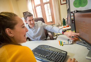 A UW student and staff member share a laugh as they have a meeting and share work on a computer.