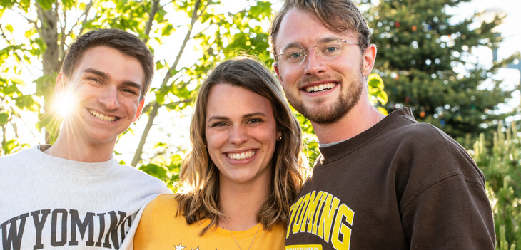 three students smiling at the camera outside