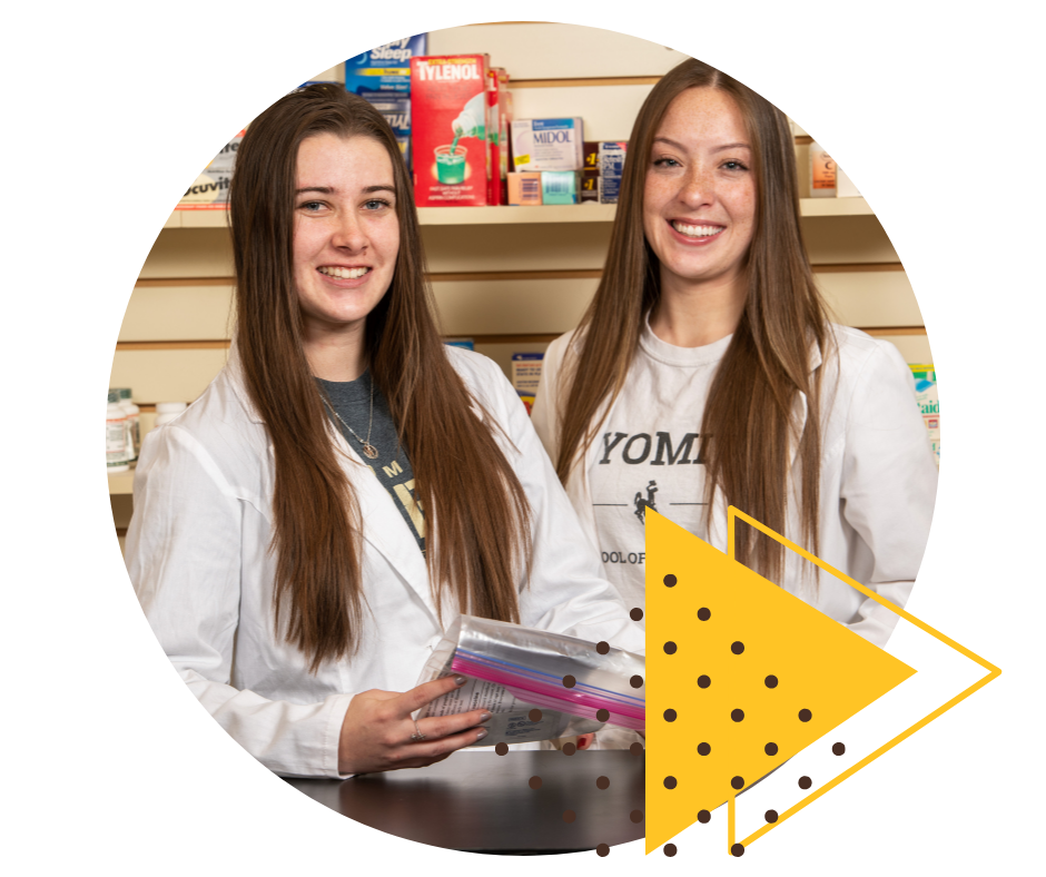 Pharmacy students in front of a wall of medications