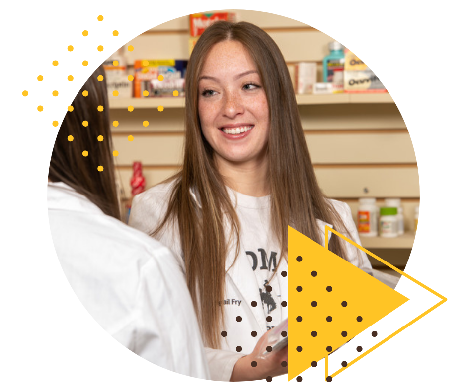 Pharmacy student in front of a wall of medications