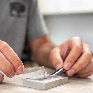Hands using needle nose forceps to pick up an aluminum tin.
