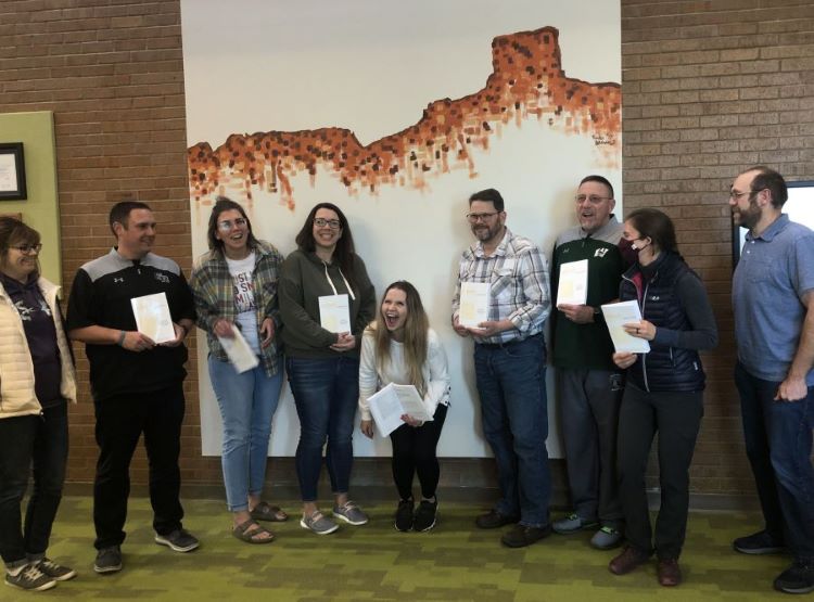 Green River High School science department, laughing and holding journals, standing in front of student art of local rock formations