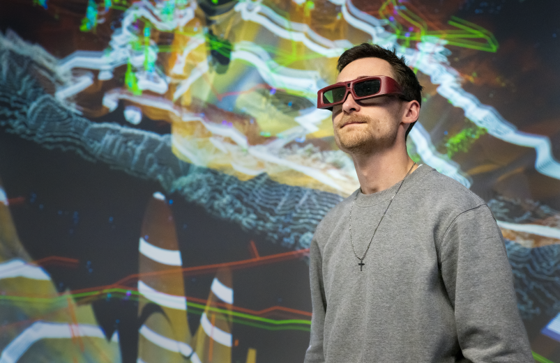 A person wearing 3D glasses with an abstract image behind them.