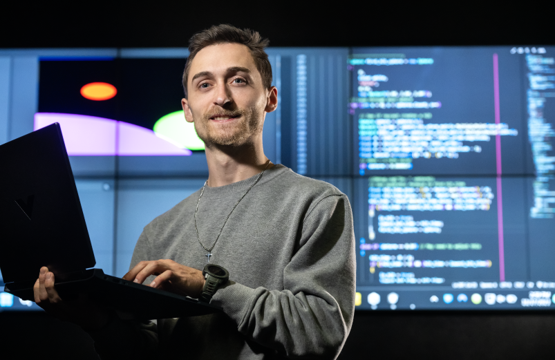 A person holding up a laptop with a projection of code behind them.