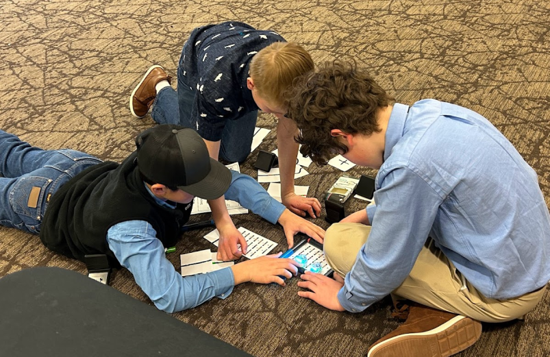 Three elementary students working on a science project on the floor.
