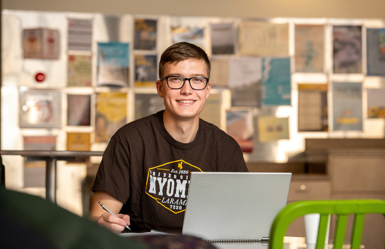 student smiling working on a laptop