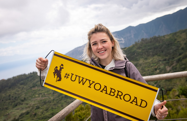 UW student holds up a UW Abroad banner in front of impressive view