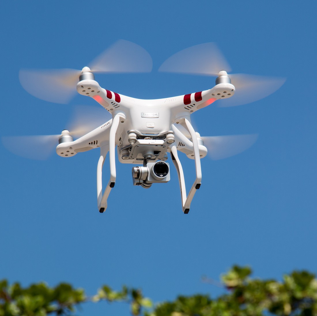 A white drone in the sky with a camera attached to the bottom of it.