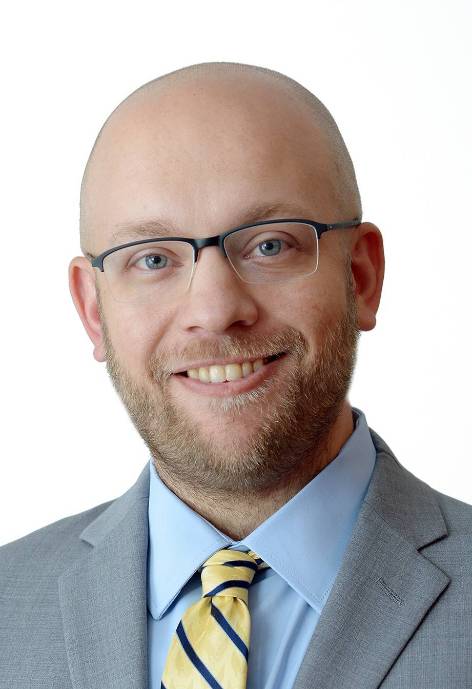 Steve Staurovski head shot wearing a bluse suit and yellow tie.