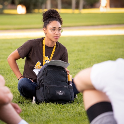 A woman sitting on grass with a backpack.