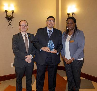 Two men and one women standing for an awards ceremony.